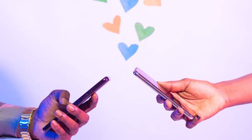 two hands holding phones messaging each other with hearts
